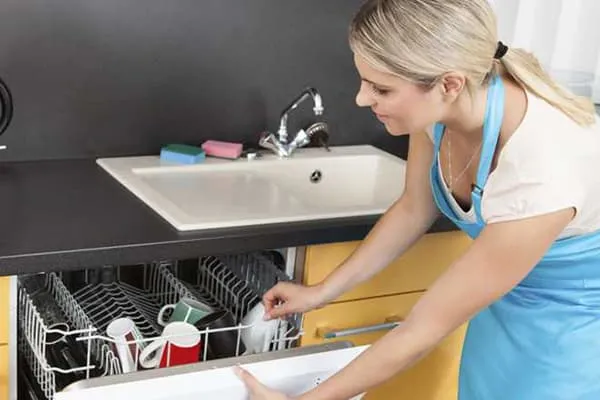 Женщина загружает посуду в посудомоечную машину
